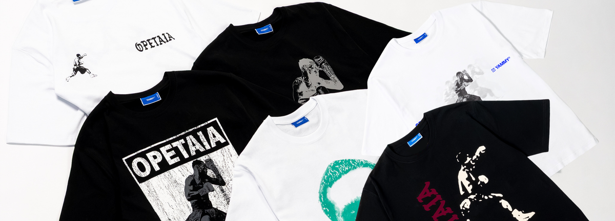 A flat-lay arrangement of multiple graphic T-shirts in black and white, featuring the word 'OPETAIA' and various stylized illustrations, on a clean white background.