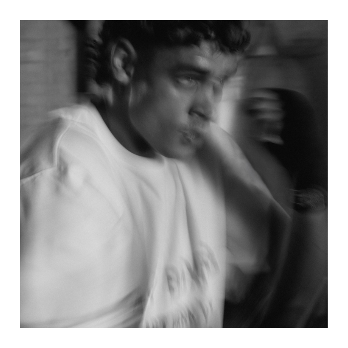Black and white square photograph of a person in a white sweatshirt, shown with motion blur and an abstract, artistic filter.