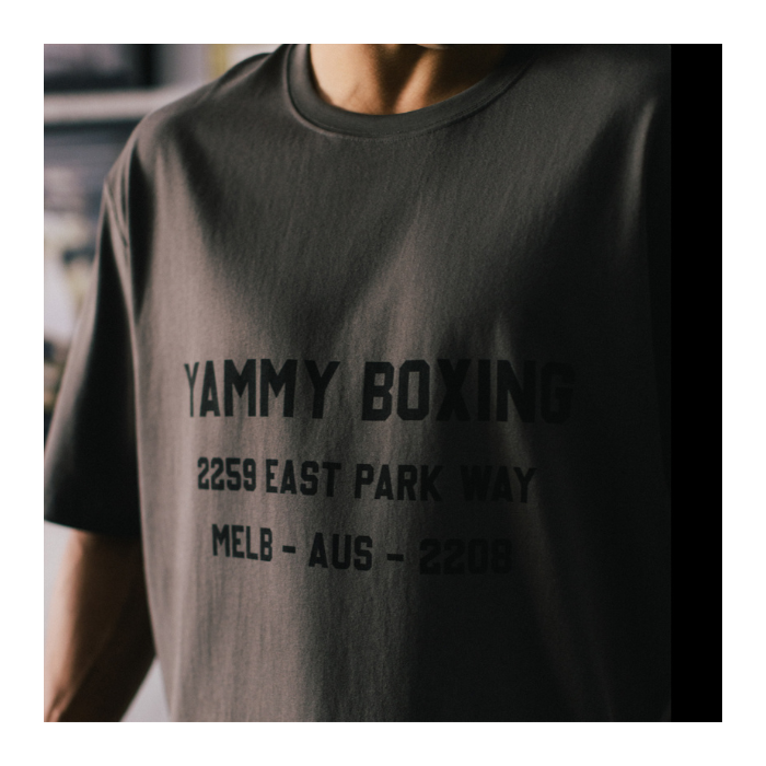 A close-up of a person wearing a dark charcoal gray t-shirt with black printed text reading 'YAMMY BOXING'