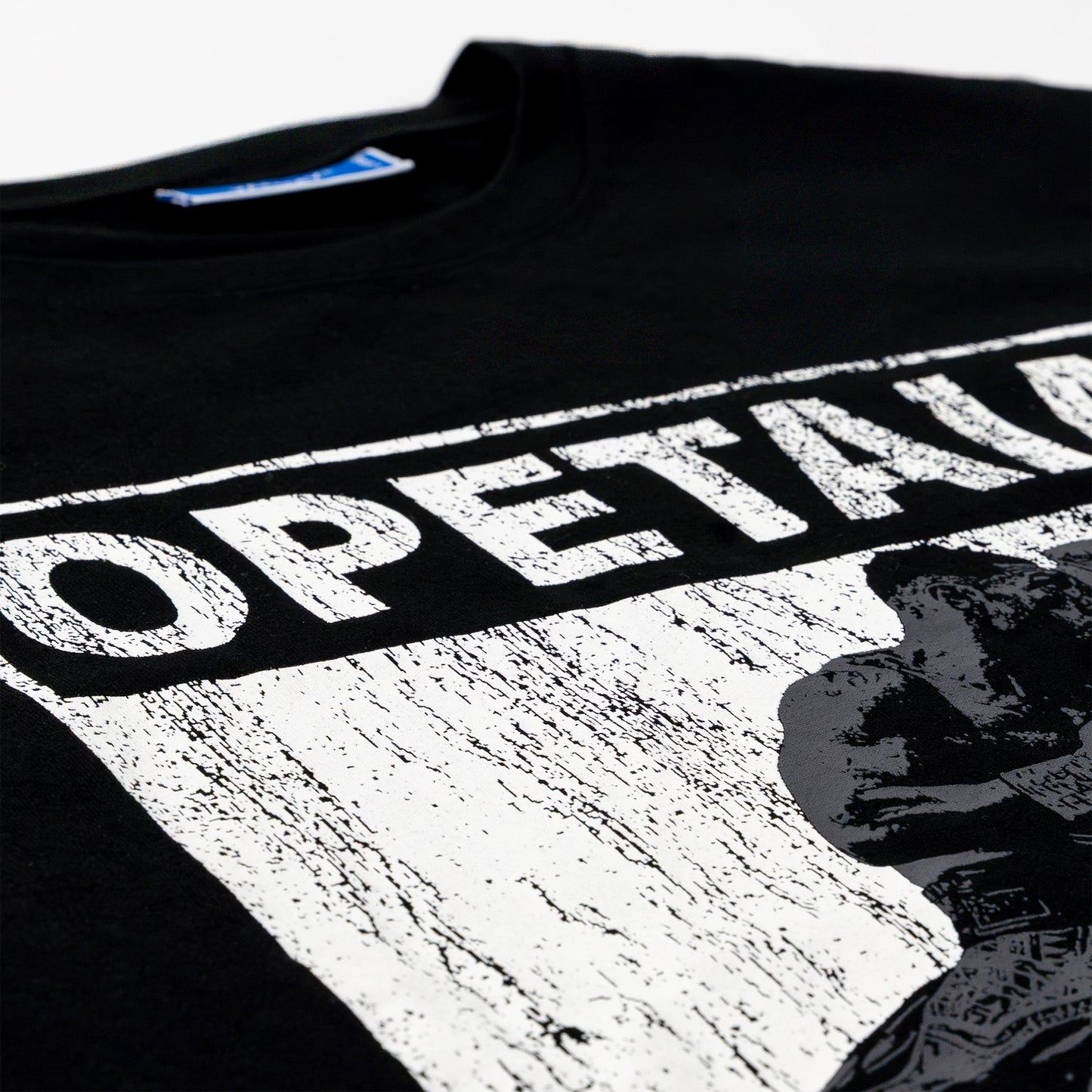 Close-up of a black T-shirt with a large distressed white graphic print reading 'OPETAIA' and a black-and-white portrait graphic on the front.