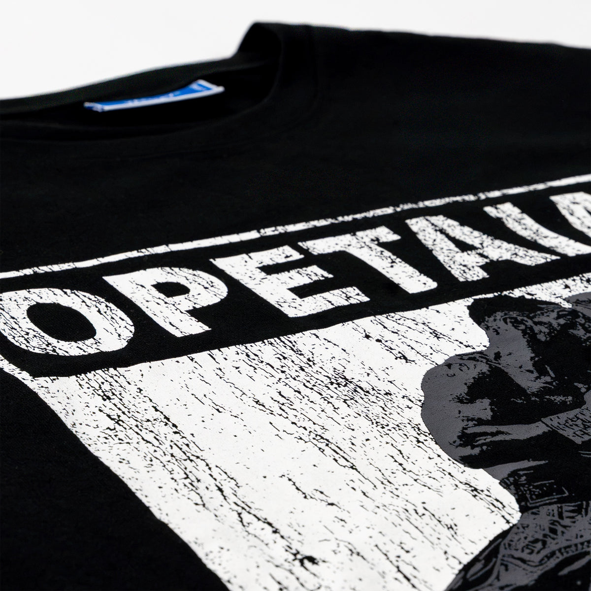 Close-up of a black T-shirt with a large distressed white graphic print reading 'OPETAIA' and a black-and-white portrait graphic on the front.
