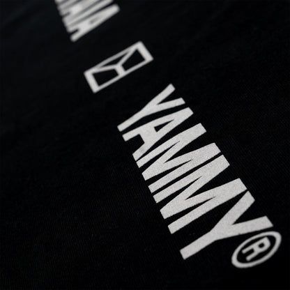 Close-up of a black fabric surface with large white YAMMY branding and a small white geometric logo printed diagonally across it.