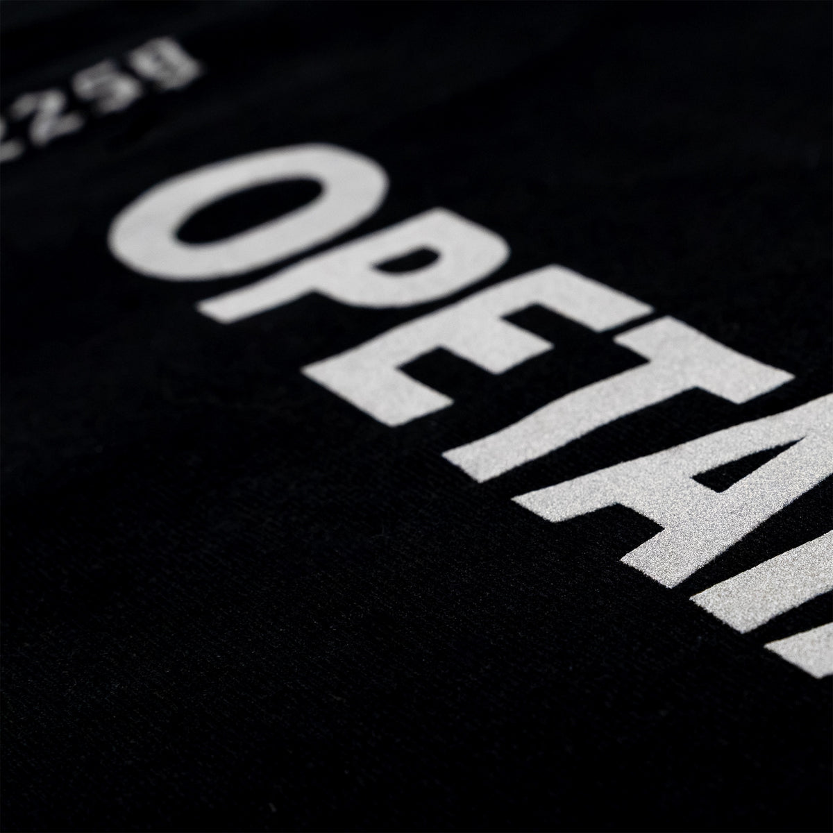Close-up of a black garment with large white printed text reading 'OPETA' and partial numbers at the top left.