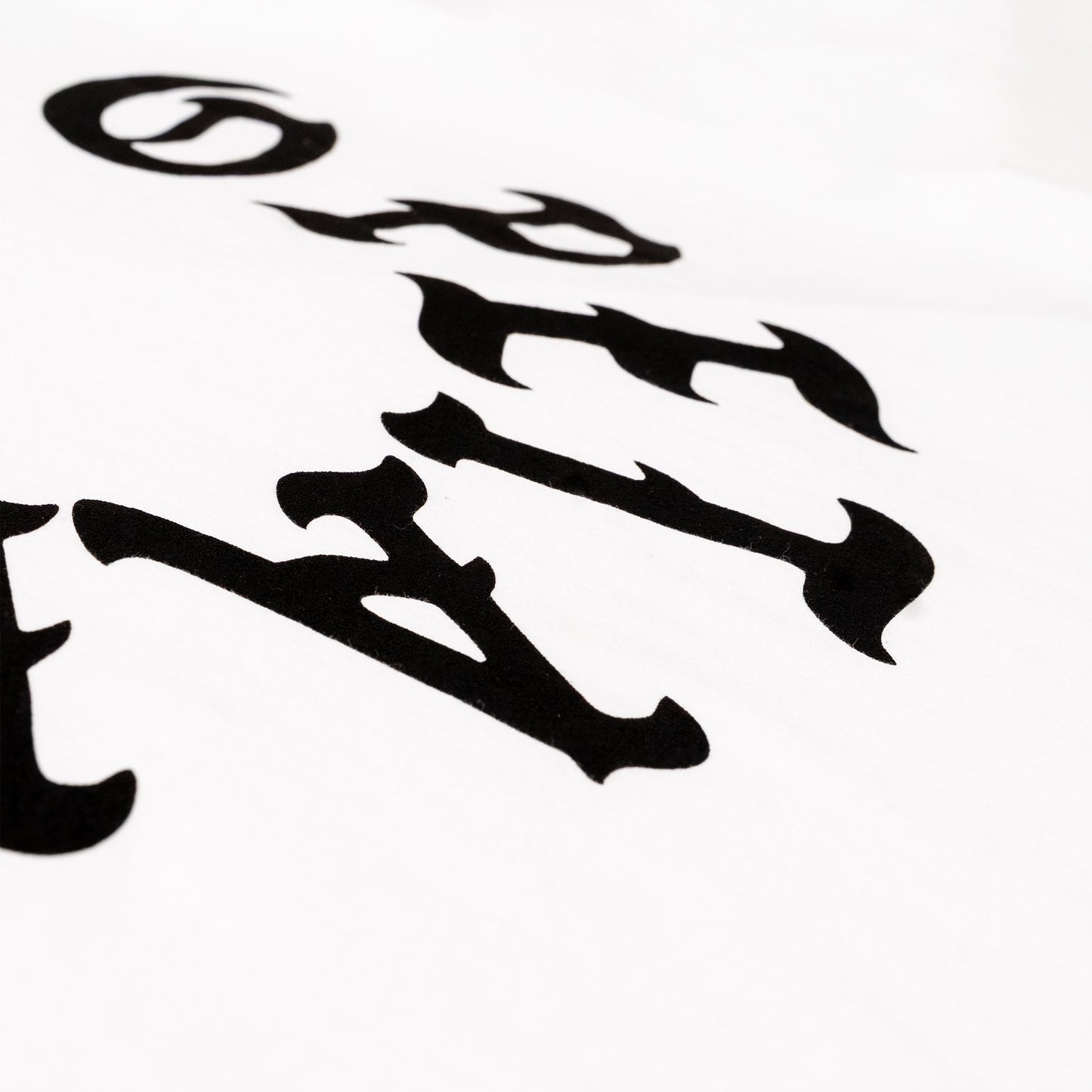 A close-up of a white fabric surface featuring a black gothic-style letter print, showing part of the word 'OPETAIA' in a bold, stylized font.