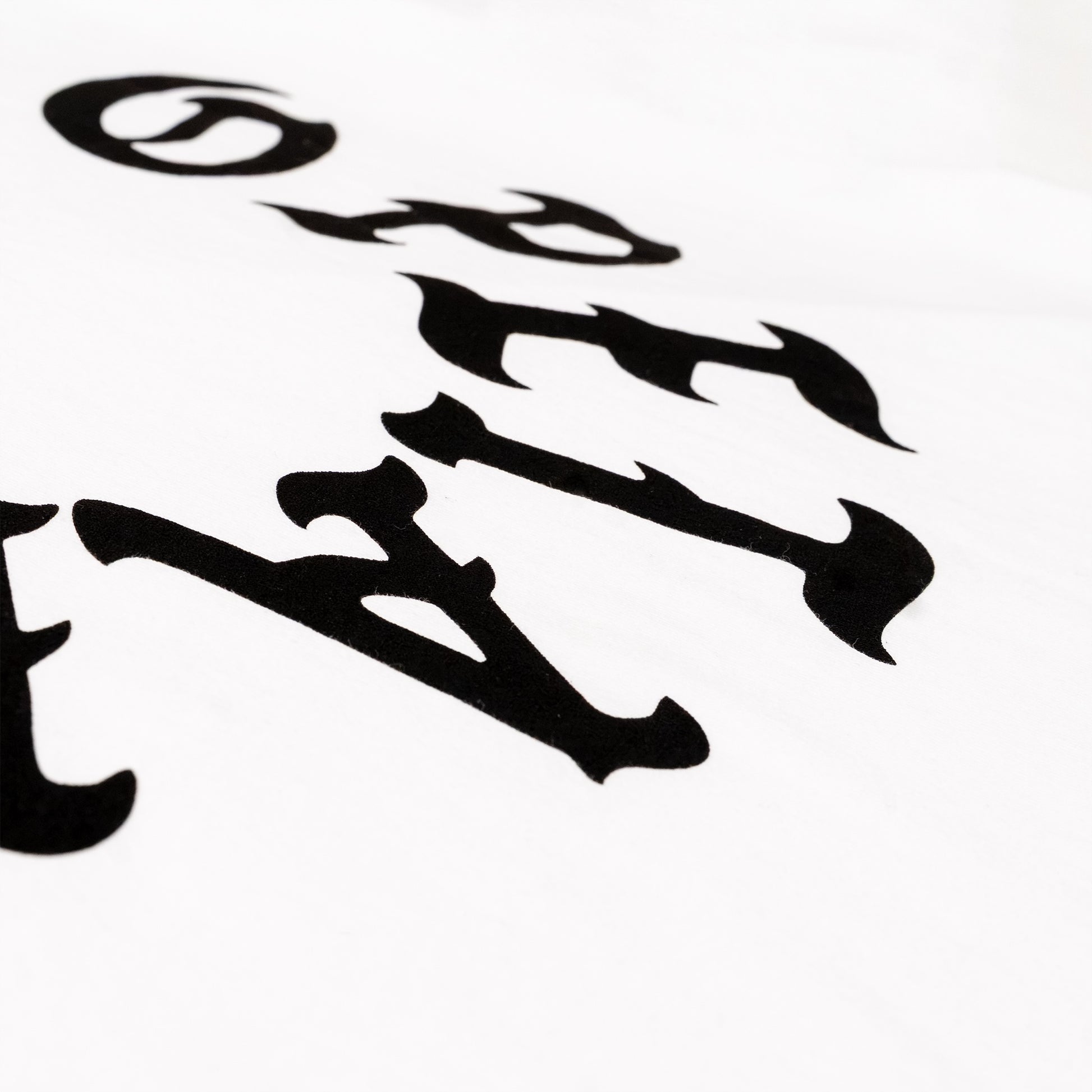 A close-up of a white fabric surface featuring a black gothic-style letter print, showing part of the word 'OPETAIA' in a bold, stylized font.