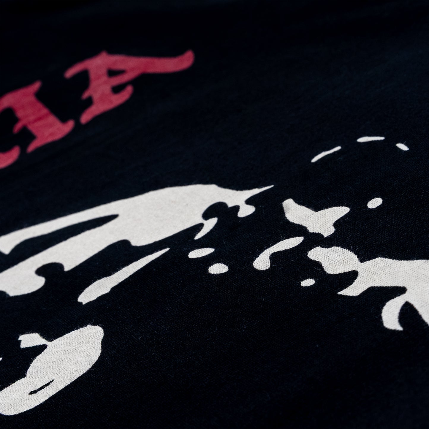 Close-up of a black graphic print featuring a white abstract shape and part of a red stylized lettering at the top left.