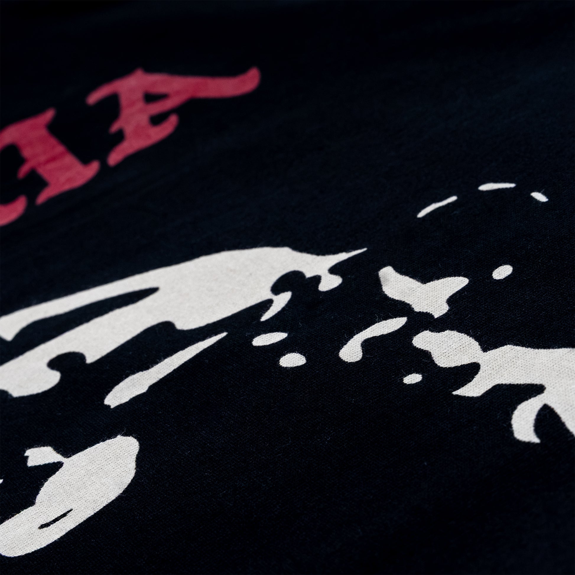 Close-up of a black graphic print featuring a white abstract shape and part of a red stylized lettering at the top left.