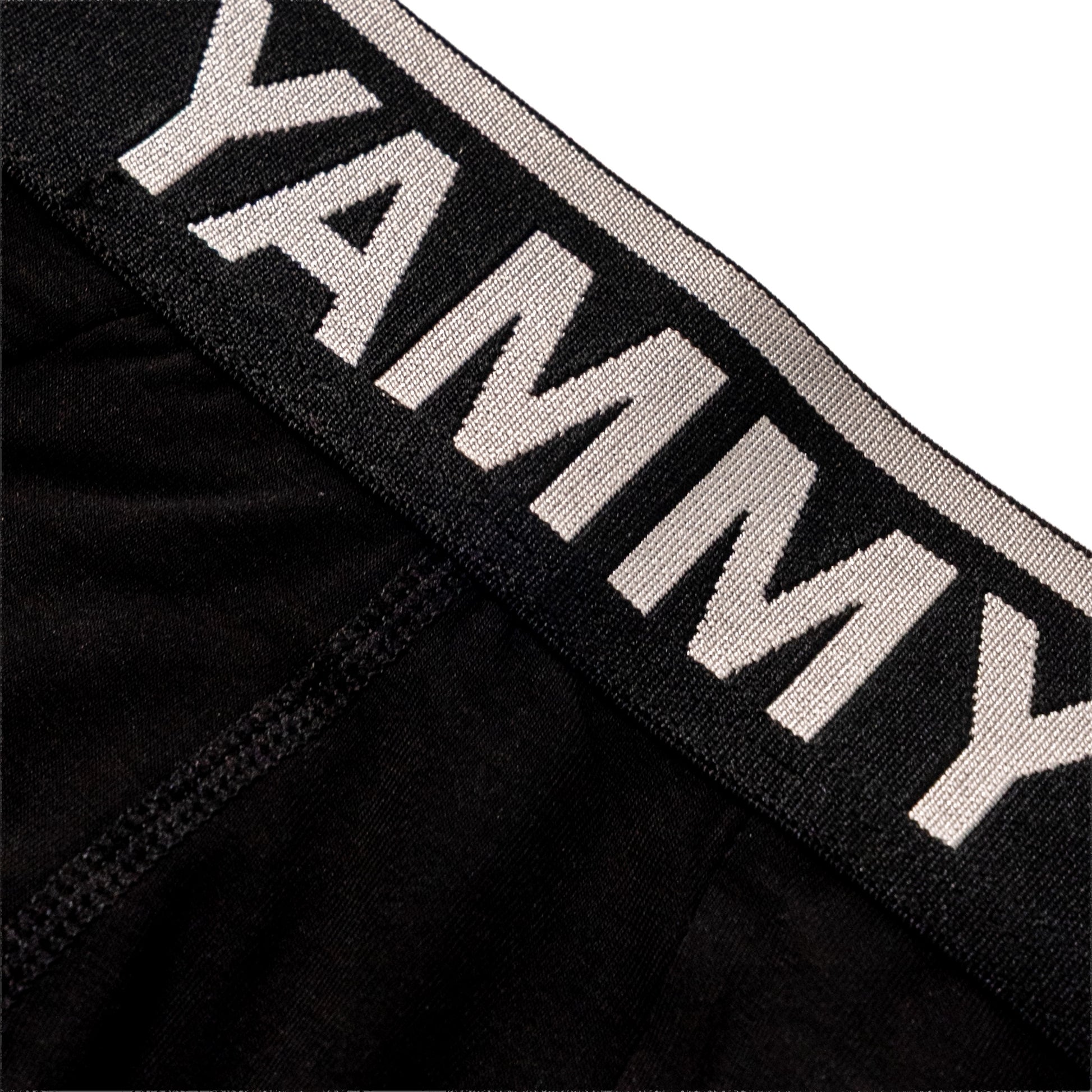 Close-up of a black underwear waistband with the brand name 'YAMMY' in large white letters on a white striped elastic band, set against a plain white background.