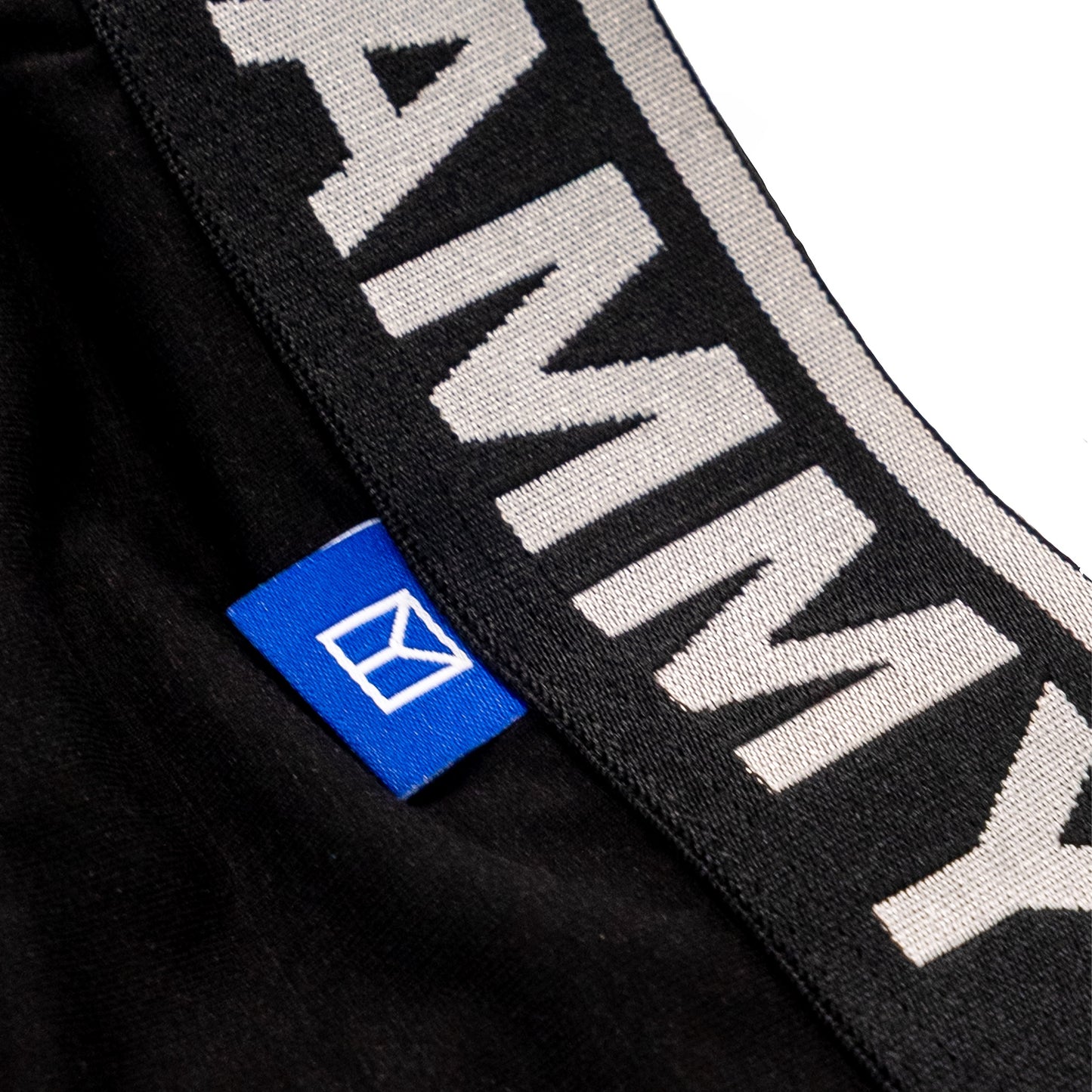 Close-up of a black knit garment with a wide black and white striped elastic band featuring large white 'YAMMY' lettering, plus a small blue fabric tag with a white logo.