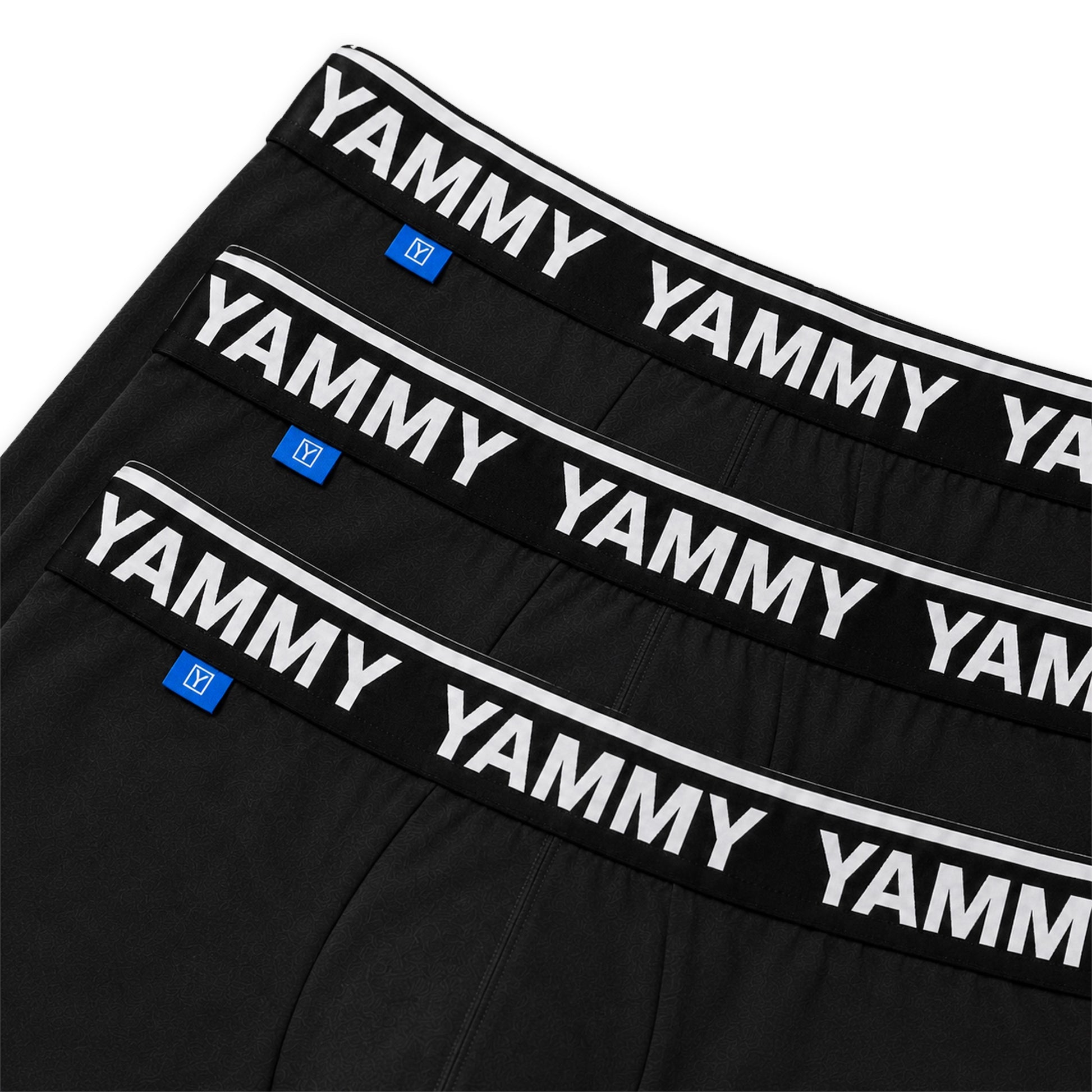 Three pairs of black boxer briefs stacked diagonally, featuring a wide black waistband with 'YAMMY' printed repeatedly in white and a small blue brand tag.