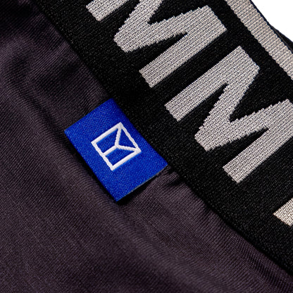 Close-up of a dark charcoal gray knit garment with a black elastic band featuring large white lettering and a small blue brand tag with a white logo.