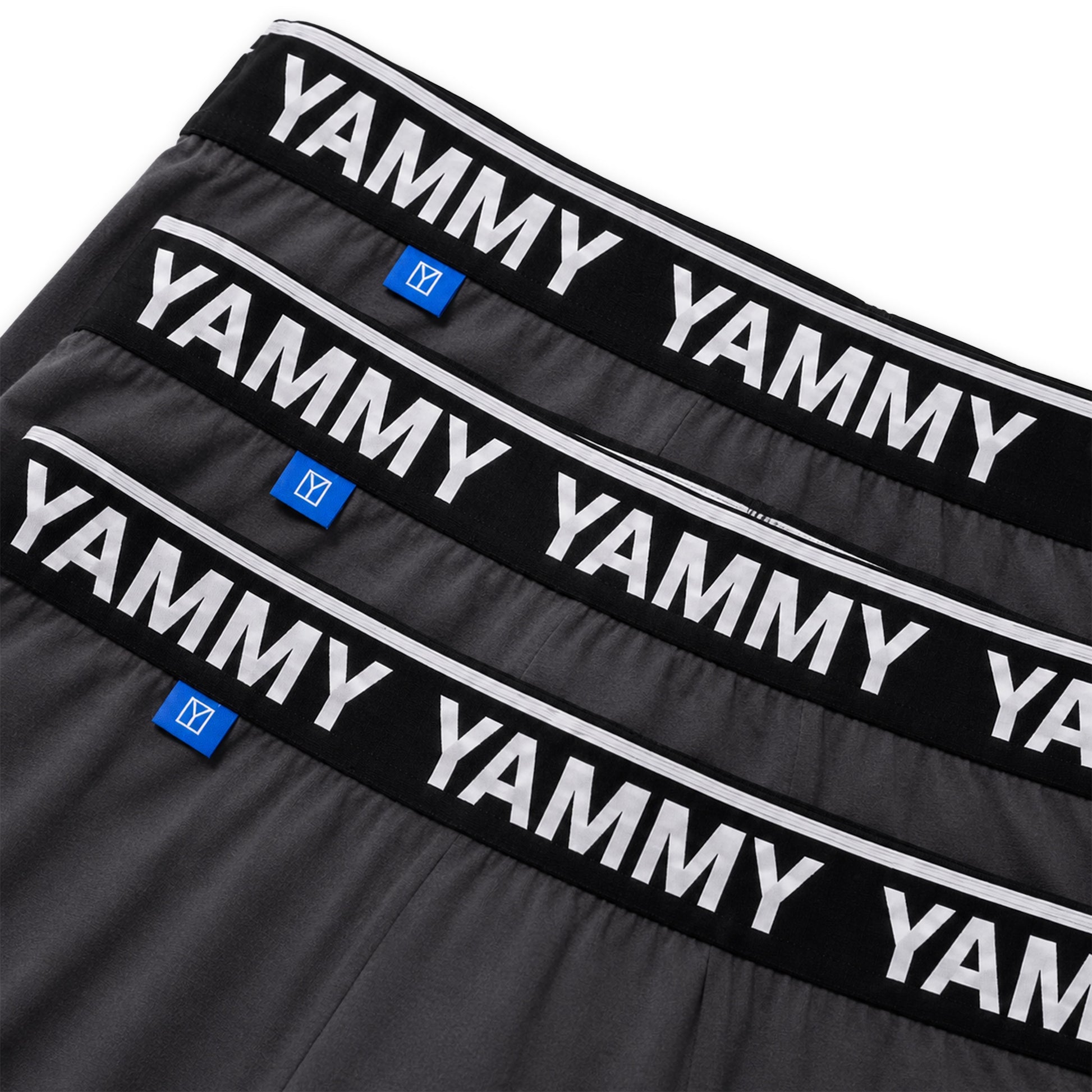 Three pairs of dark gray boxer briefs stacked diagonally, showing black elastic waistbands with white 'YAMMY' branding and small blue size tags.