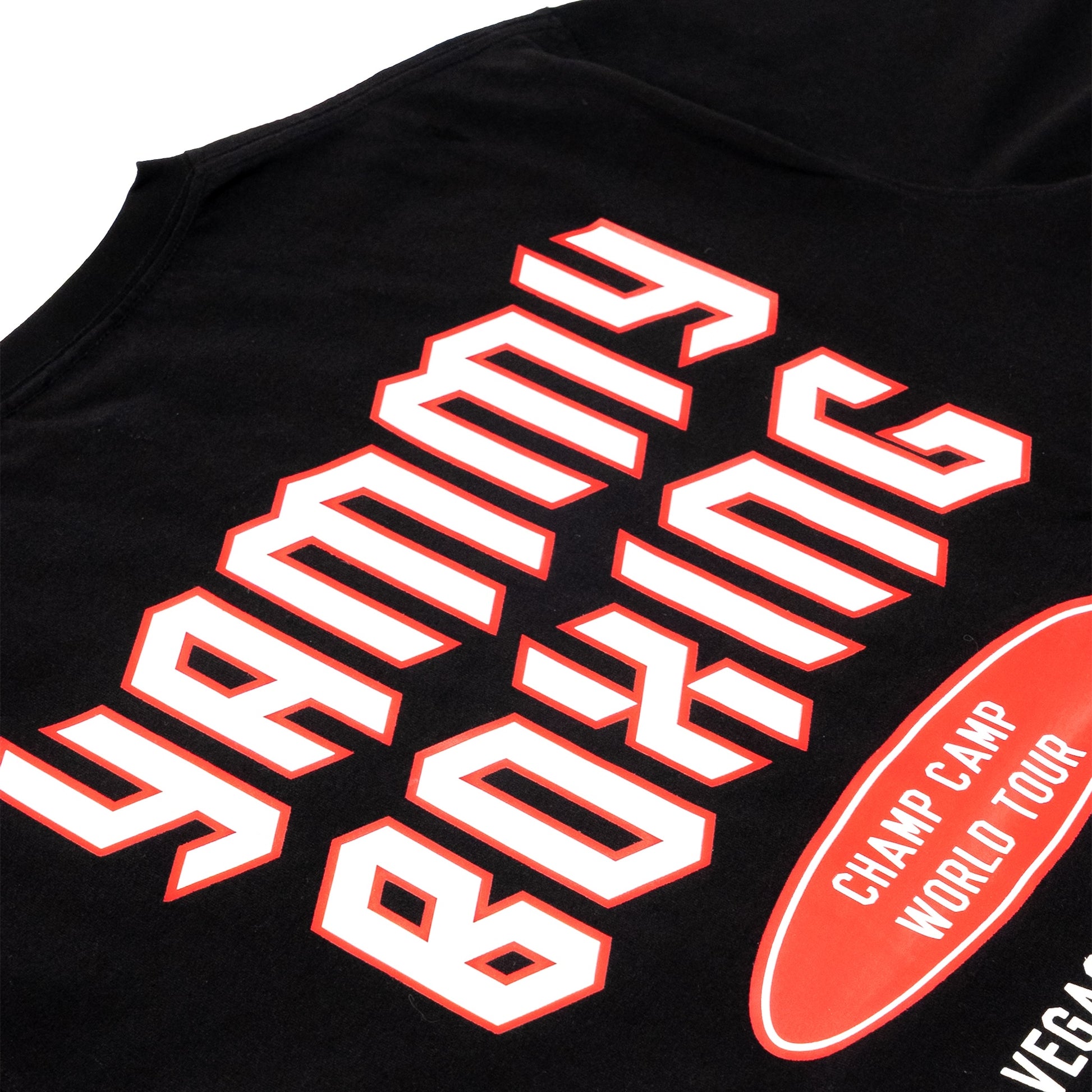 Close-up of a black tank top featuring a large white 'YAMMY BOXING' graphic with red outlines, alongside a red oval badge reading 'CHAMP CAMP WORLD TOUR' and partial 'VEGAS' text.