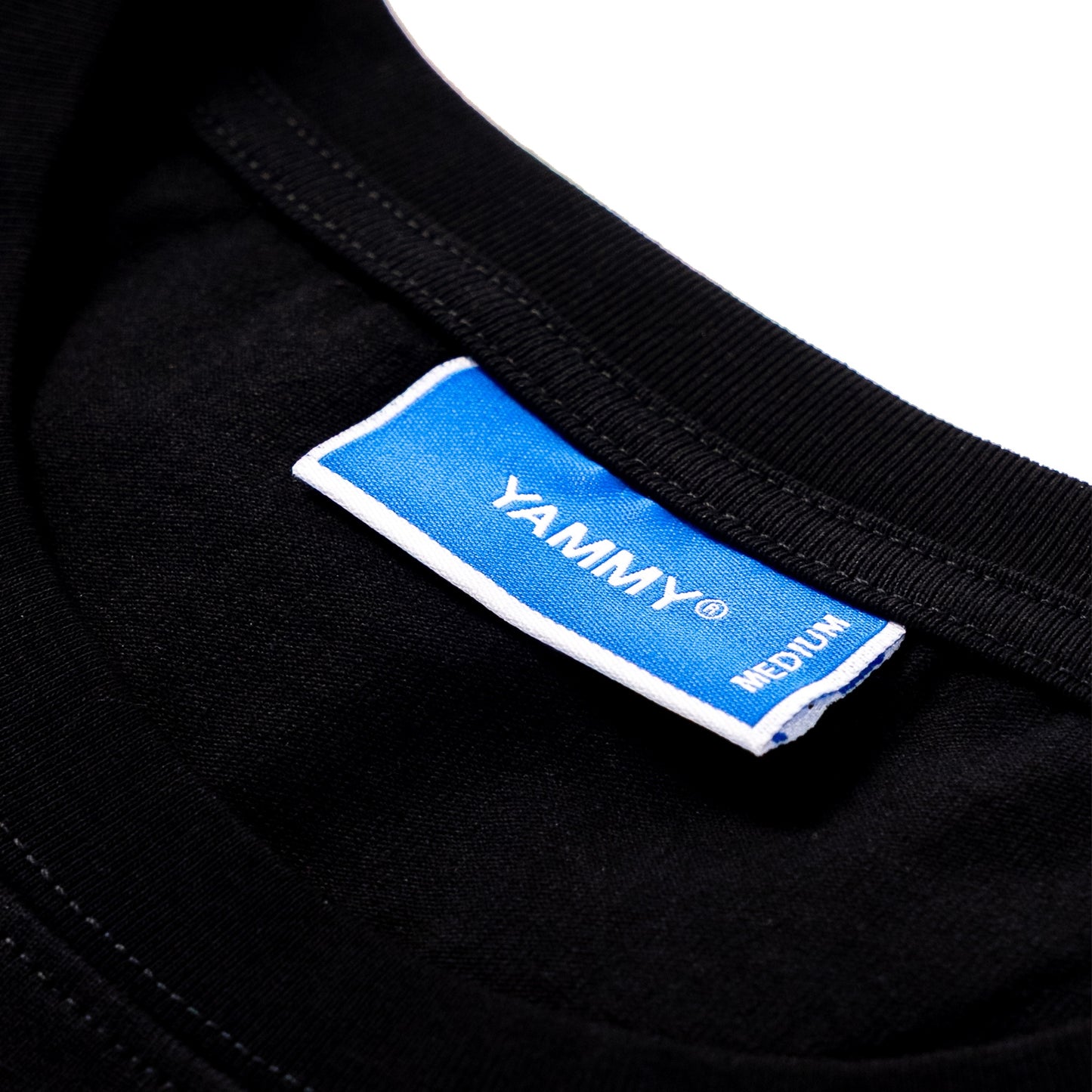 Close-up of a black garment neck label with a blue and white tag reading YAMMY and MEDIUM.