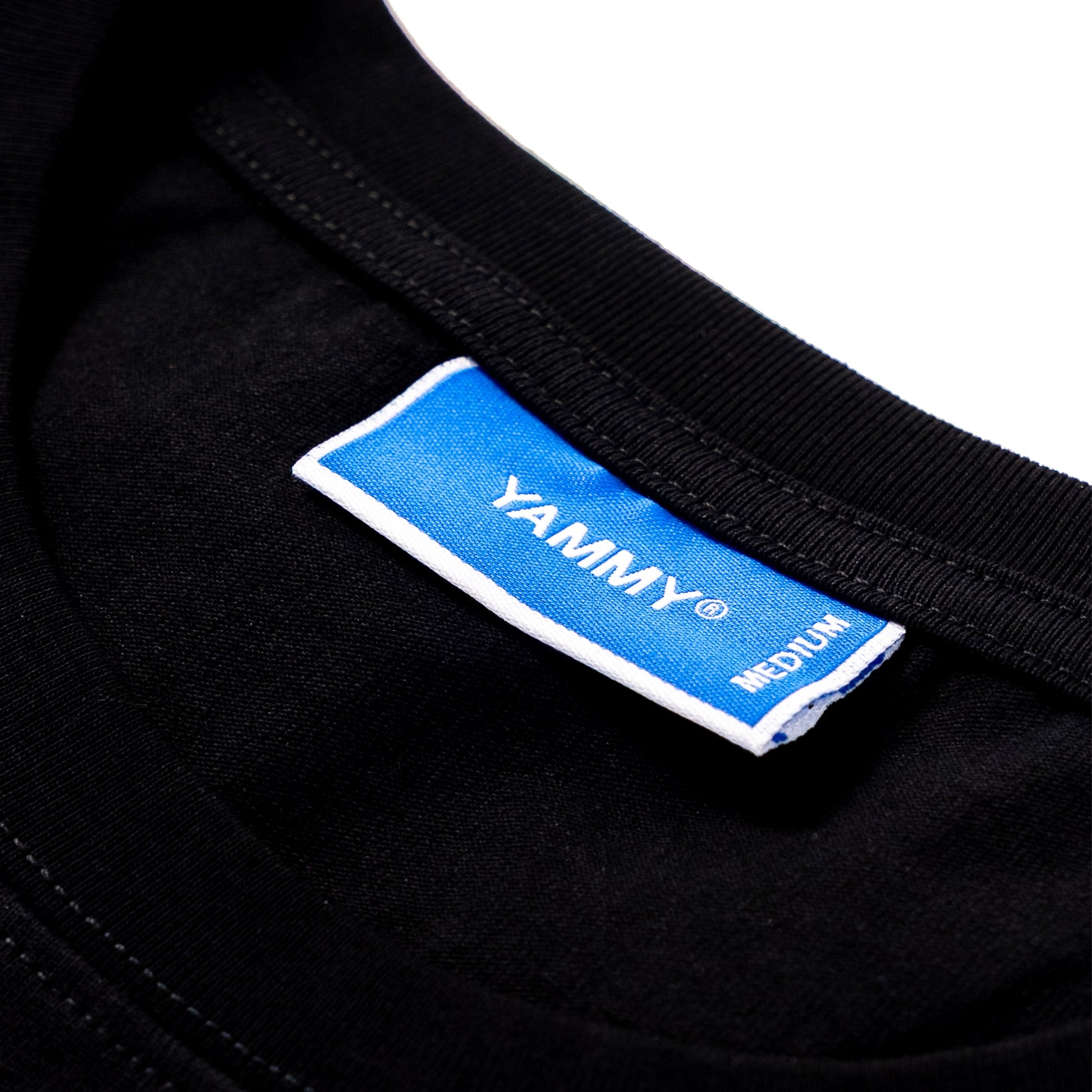 Close-up of a black garment neck label with a blue and white tag reading YAMMY and MEDIUM.