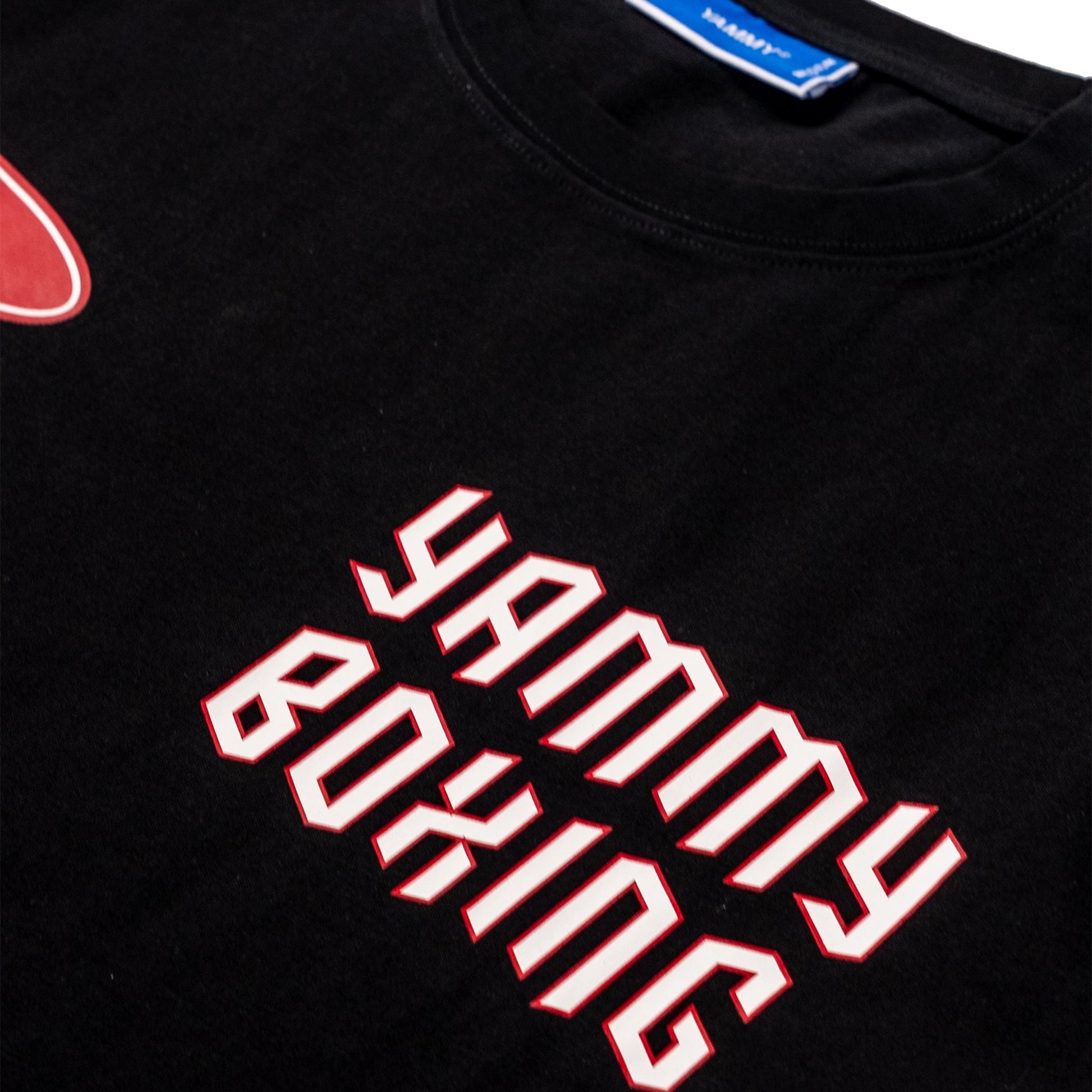 Close-up of a black t-shirt featuring the words 'YAMMY BOXING' in a stylized white font with a red outline. A blue tag with 'YAMMY' is visible inside the collar.