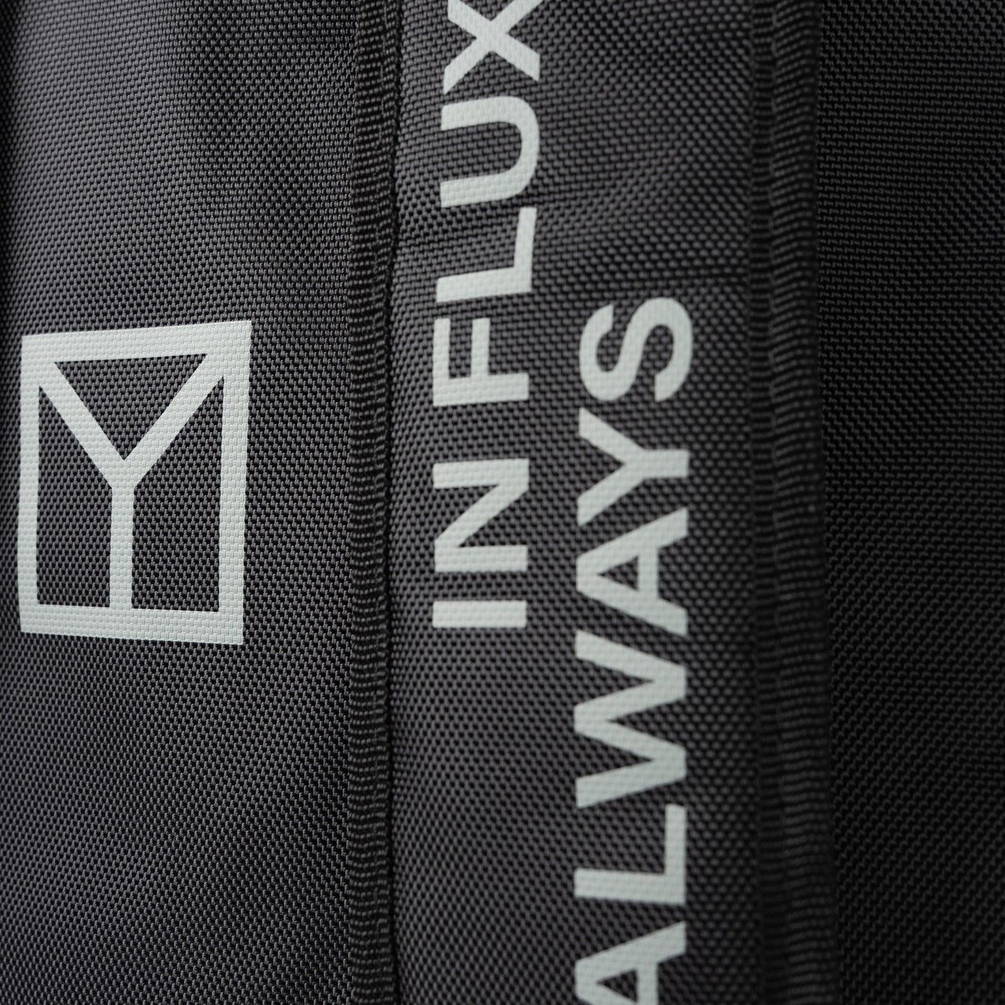 Close-up of a black textured fabric item featuring a white geometric logo and vertical white text reading 'ALWAYS IN FLUX'