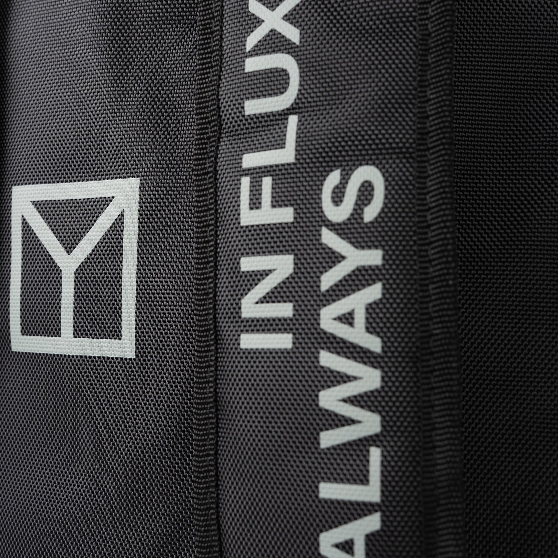 Close-up of a black textured fabric item featuring a white geometric logo and vertical white text reading 'ALWAYS IN FLUX'