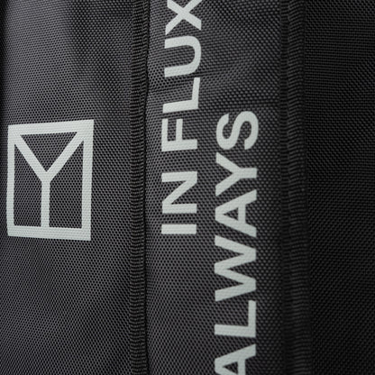 Close-up of a black textured fabric item featuring a white geometric logo and vertical white text reading 'ALWAYS IN FLUX'