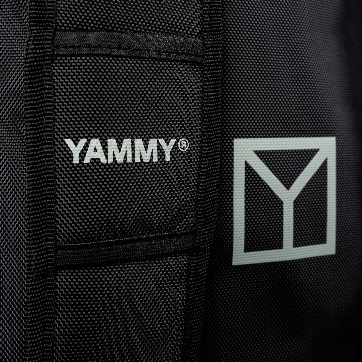 Close-up of a black textured fabric product with white YAMMY branding and a white geometric Y logo on the side.