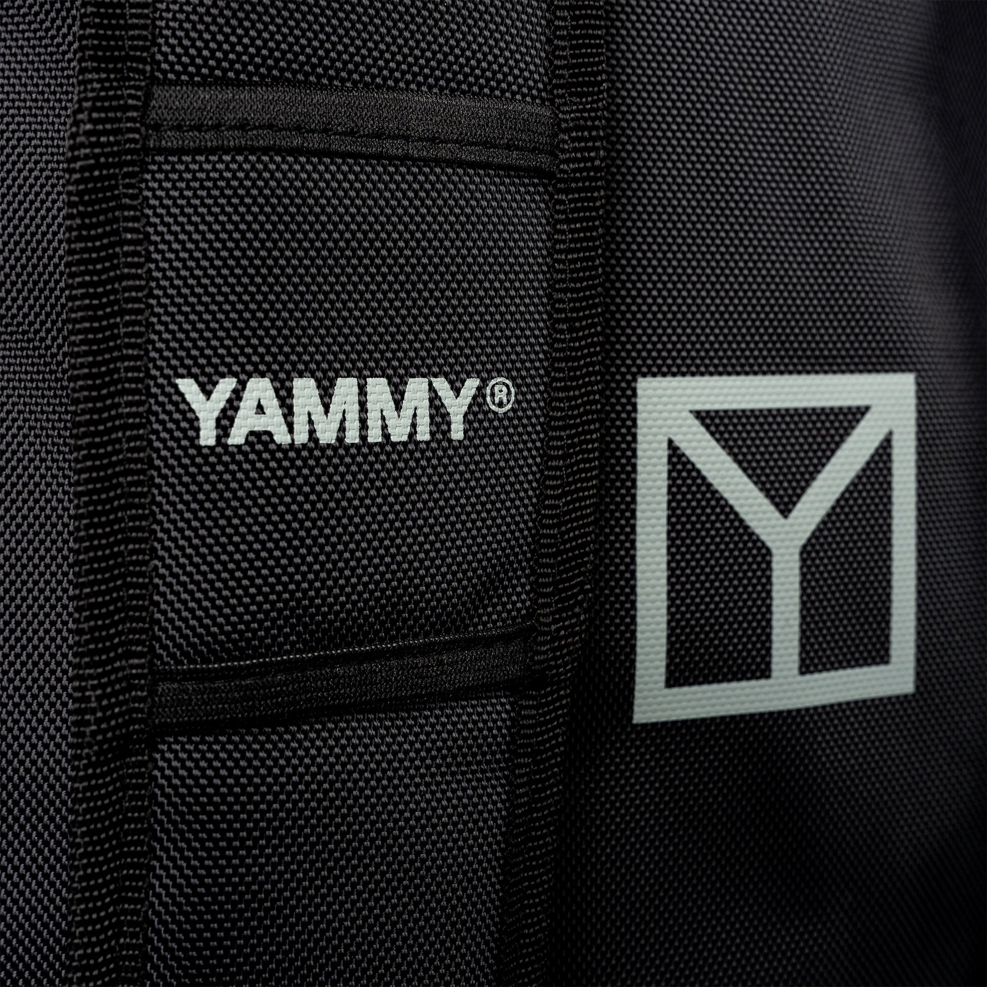 Close-up of a black textured fabric product with white YAMMY branding and a white geometric Y logo on the side.