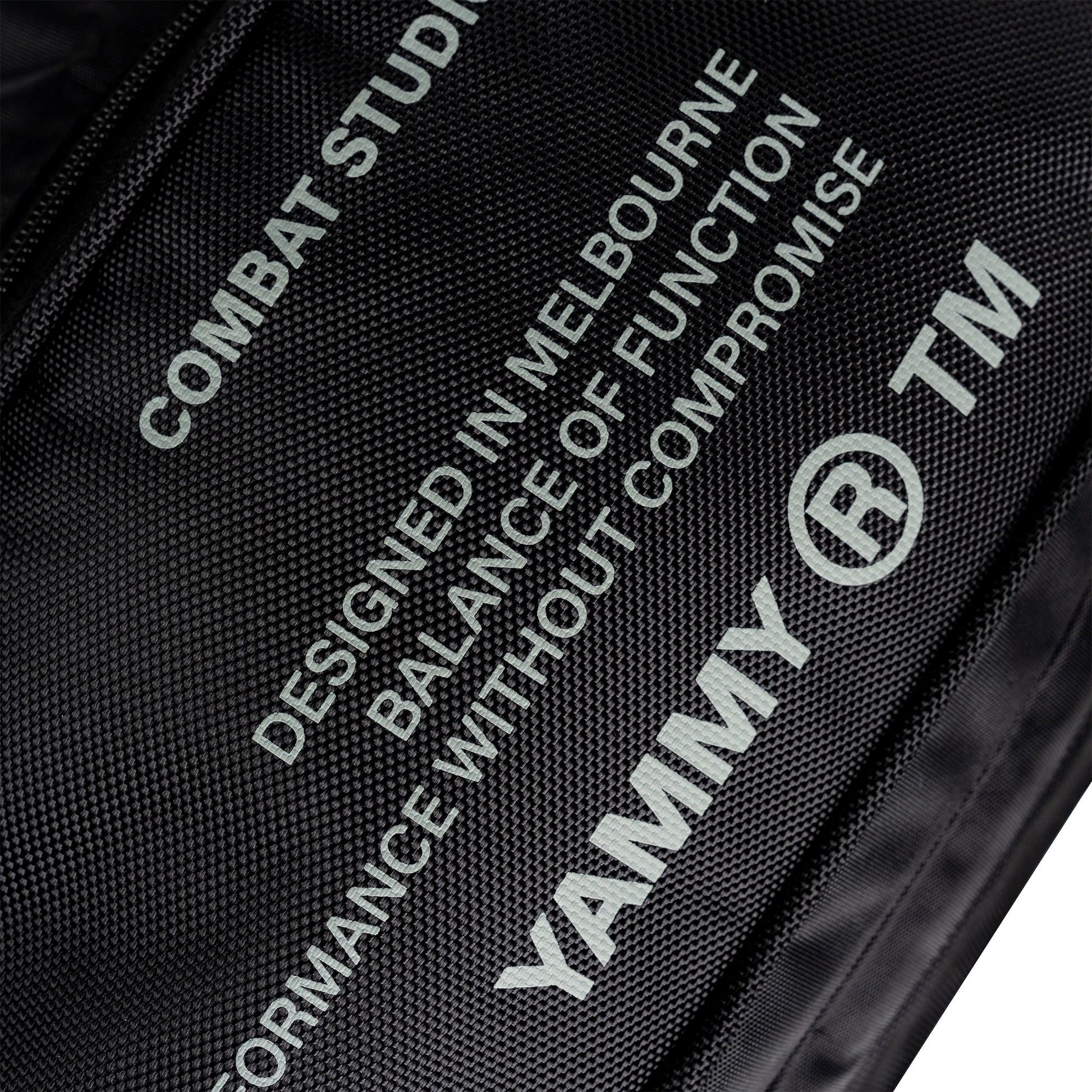 Close-up of a black textured fabric bag with white printed text and logos, including 'YAMMY' and 'TM' alongside design copy.