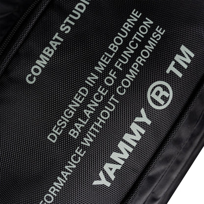 Close-up of a black textured fabric bag with white printed text and logos, including 'YAMMY' and 'TM' alongside design copy.