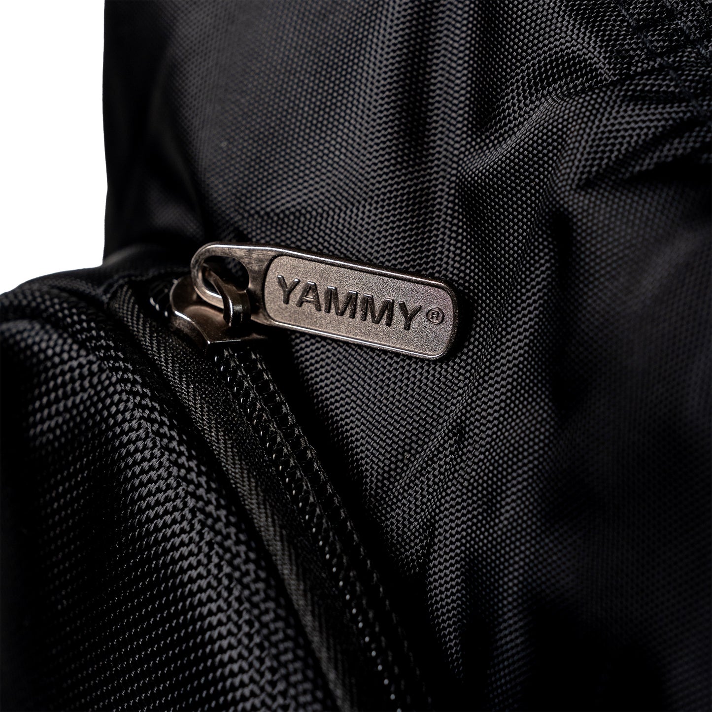 Close-up of a black textured nylon bag with a silver metal zipper pull tab engraved with the brand name 'YAMMY'.