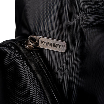 Close-up of a black textured nylon bag with a silver metal zipper pull tab engraved with the brand name 'YAMMY'.