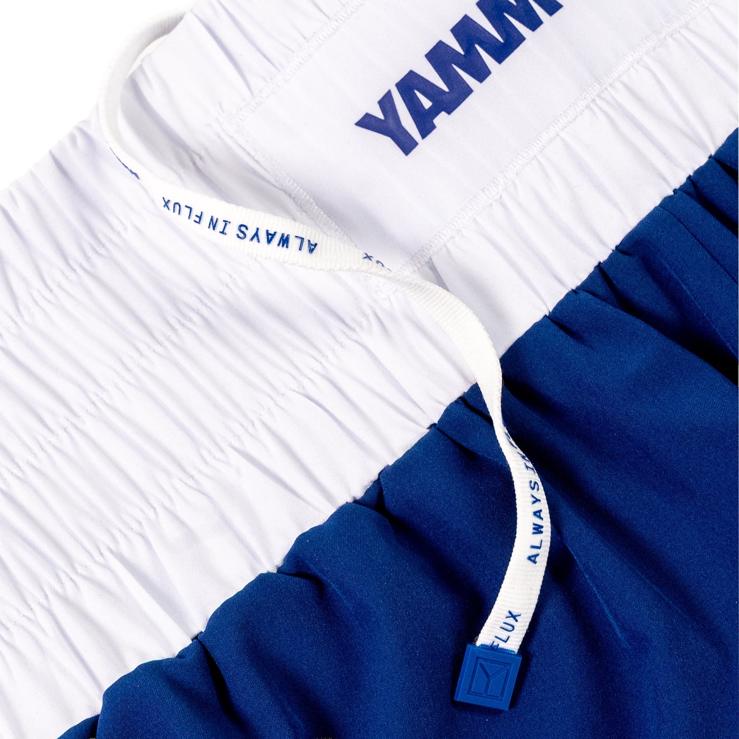 Close-up of athletic shorts with a white upper section and a royal blue lower section, featuring a white drawstring with blue text and a blue logo tab.