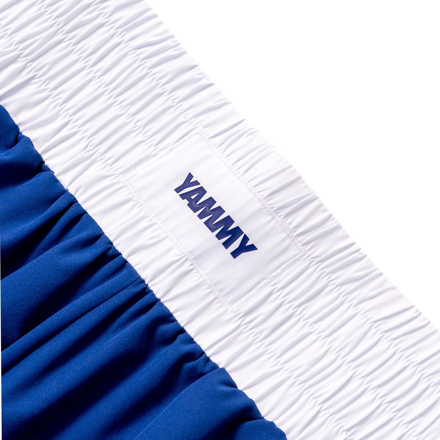 Close-up of athletic shorts showing a white elastic waistband with the brand name 'YAMMY' in navy blue, paired with a royal blue fabric body.