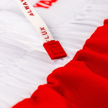 Close-up of a white drawstring with red text reading 'ALWAYS IN FLUX' and a red plastic toggle, attached to a red and white garment fabric.