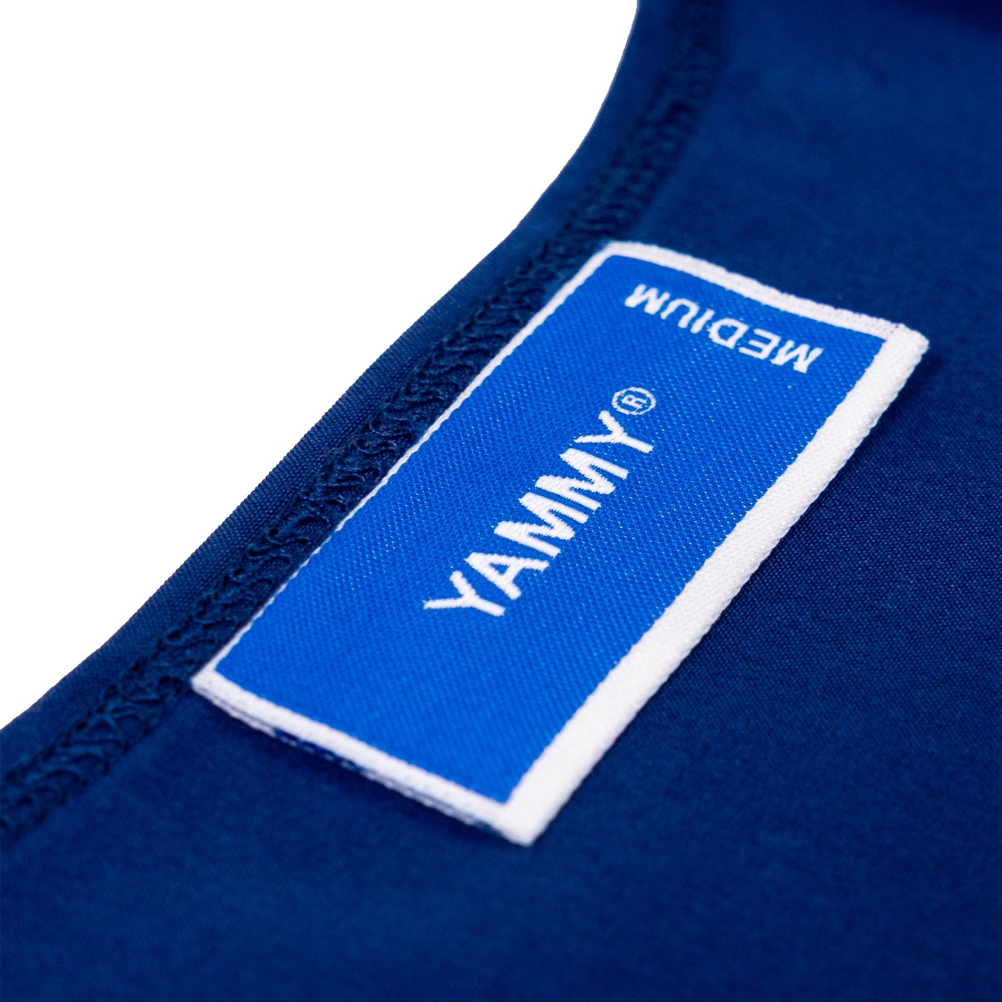 Close-up of a blue fabric garment label with white trim and white text reading 'YAMMY' and 'MEDIUM', attached to dark blue clothing on a white background.
