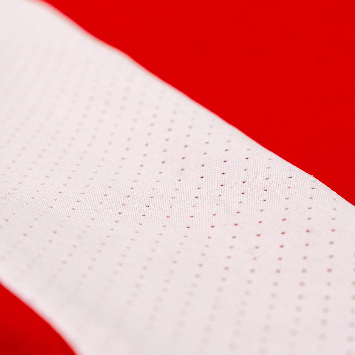 Close-up of a white athletic fabric strip with a perforated mesh pattern, set against a solid red background.