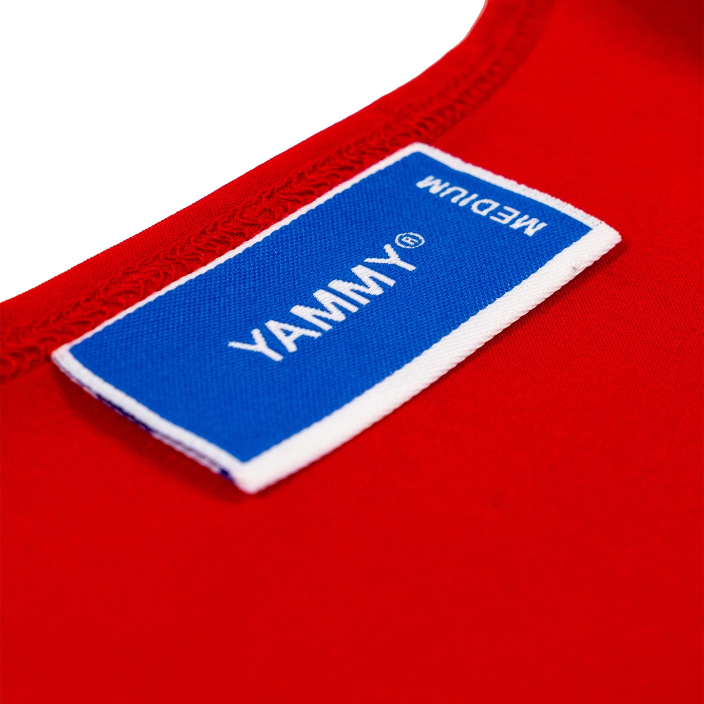 Close-up of a red garment with a blue and white fabric label reading YAMMY and MEDIUM.