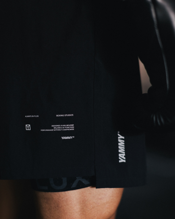 Close-up of a person wearing black athletic shorts with white printed text and logos, including 'YAMMY' on the side and small text near the hem.