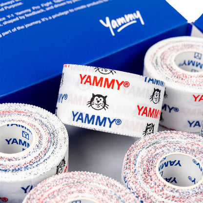 Several rolls of white athletic tape with red and blue speckled edges and repeated YAMMY logos and Hector cat icons, arranged in front of a blue branded box.