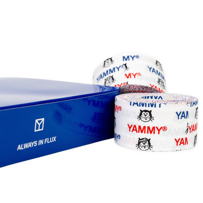 Two rolls of white YAMMY brand tape with red and blue lettering and a black cat logo, displayed next to a blue box with 'ALWAYS IN FLUX' text on a white background.
