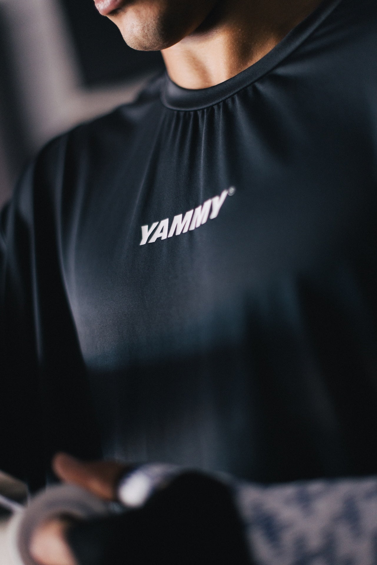 A close-up of a person wearing a black athletic long-sleeve shirt with the brand name 'YAMNY' printed in white across the chest.