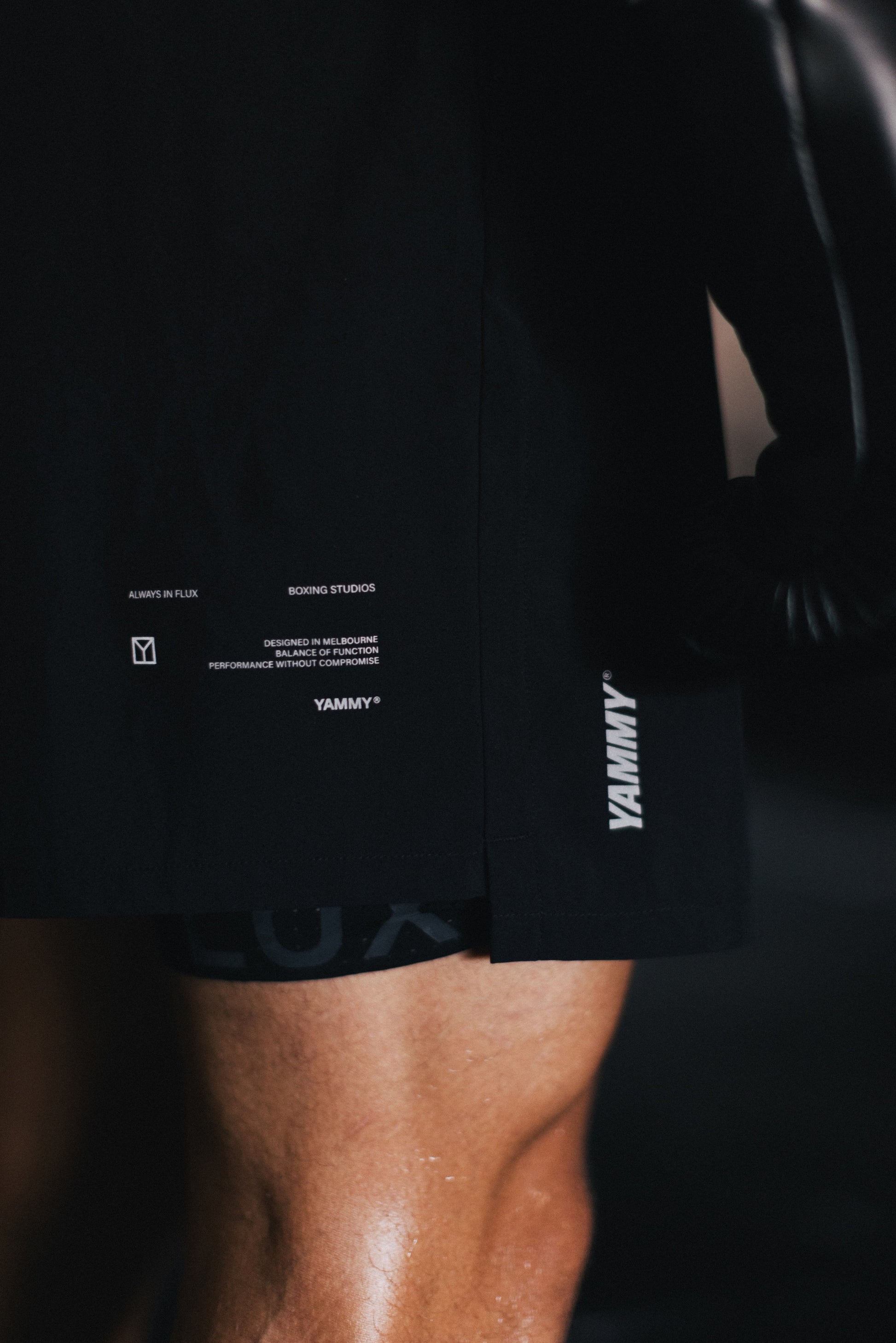 Close-up of a person wearing black athletic shorts with white printed branding and text details, including 'YAMMY' on the side and small text near the hem.